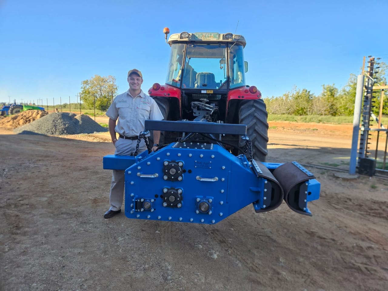 Jacobus beside a blue SMJ tree shaker attached to a red tractor in an orchard
