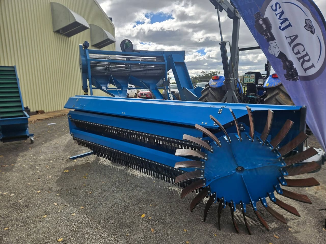 Blue SMJ 3m Orchard Sweeper with brush rows and rotor, hitched next to a tractor