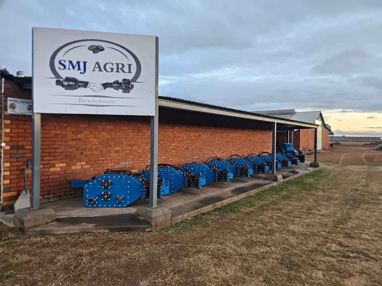 SMJ Agri premises with a row of blue implements under the SMJ Agri sign